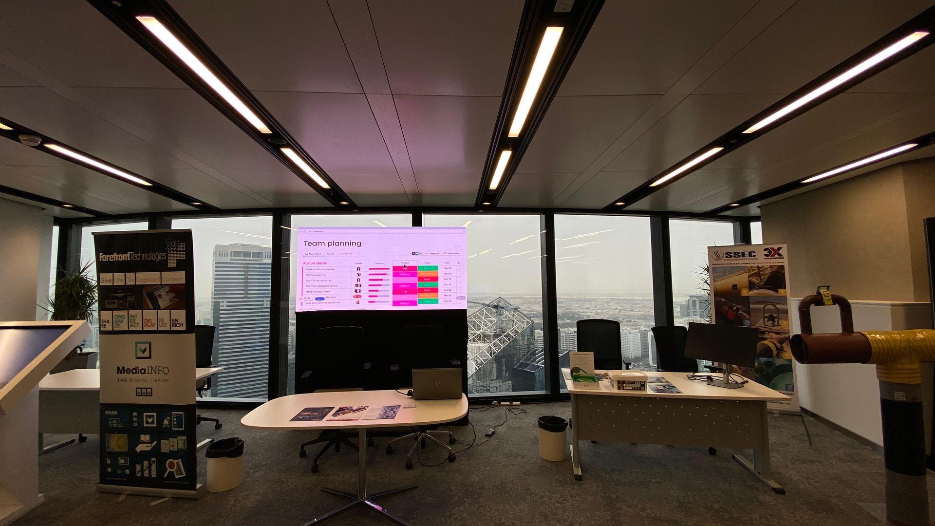 Modern office with large windows overlooking a city, featuring presentation screens and promotional banners on display.